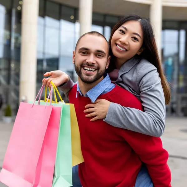 一个微笑的国际家庭一起购物、拥抱、在大商场前提着礼品袋的画像 — 图库照片