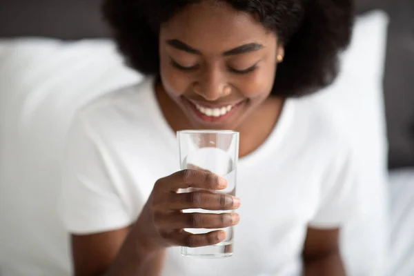 Junge schwarze Frau nimmt Glas Wasser im Bett — Stockfoto
