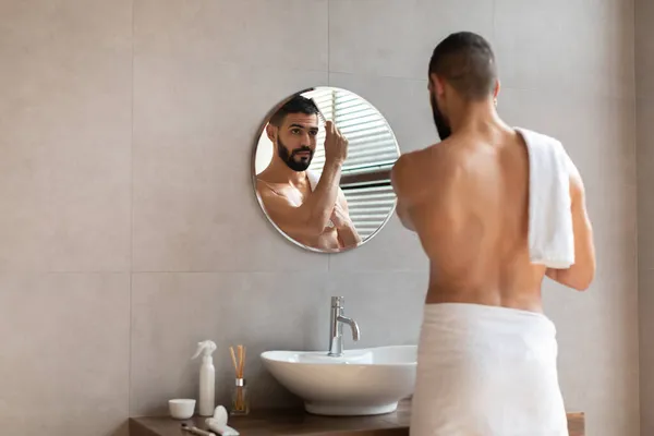 Vista trasera del tipo mirando en espejo cepillando el pelo — Foto de Stock