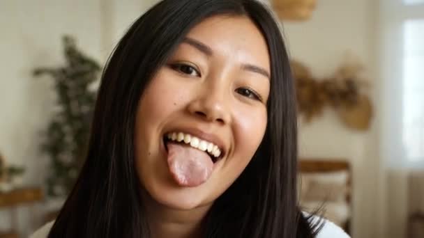 Молода грайлива азіатська леді обманює, стирчить язиком і танцює на камеру вдома, граючи з волоссям — стокове відео