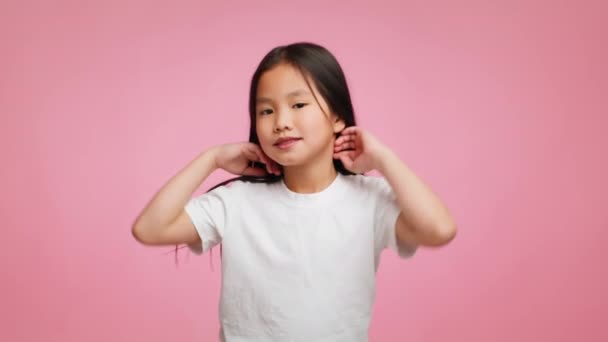 Азиатская девочка играет с длинными волосами на розовом фоне — стоковое видео