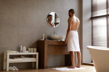 Kendine güvenen genç bir Arap aynaya bakıyor, çenesine dokunuyor.