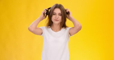 Dinamik müzik konsepti. Genç, neşeli bir kadın kulaklık takıyor ve sarı stüdyo arka planında dans etmeye başlıyor.