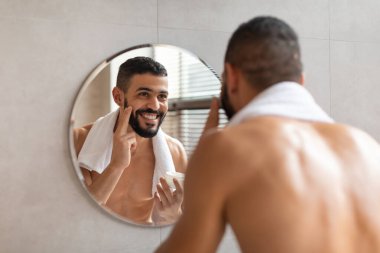 Mutlu adam aynaya bakıyor ve yüzüne krem sürüyor.