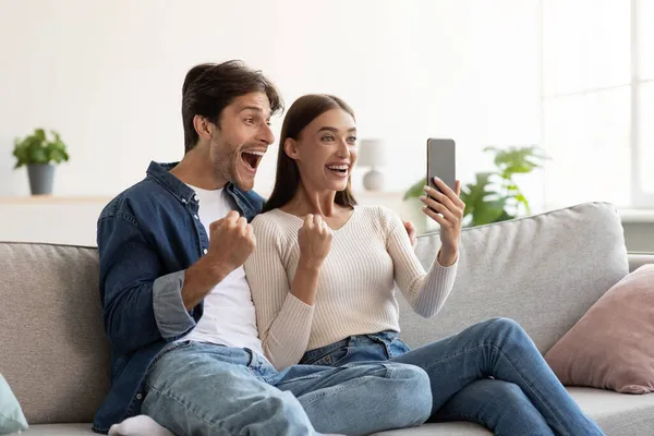 Mutlu Kafkasyalı genç karı ve koca çevrimiçi zafere seviniyor ve akıllı telefona birlikte bakıyoruz. — Stok fotoğraf