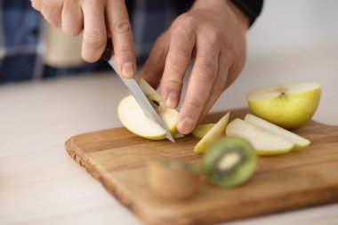 Olgun adam, mutfakta meyve salatası yaparken tahta tahtada taze elma ve kivi kesiyor, yakın plan.