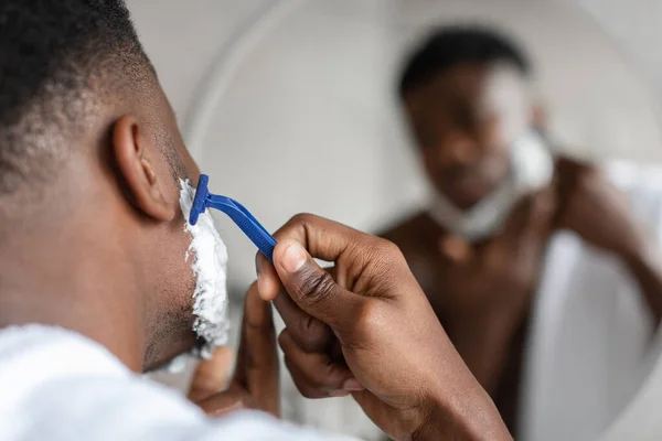 Fekete férfi borotválkozás arc biztonsági borotva a fürdőszobában, közelkép — Stock Fotó