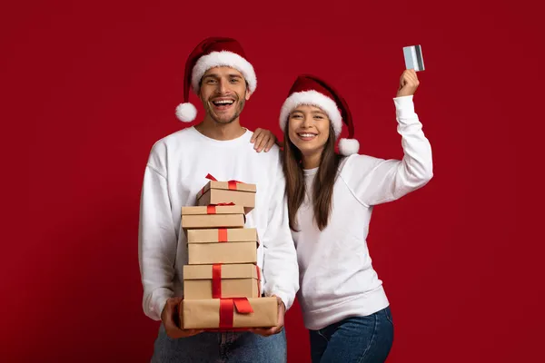 クリスマスショッピング。クレジットカードとギフトのスタックを持つ幸せな若いカップル — ストック写真