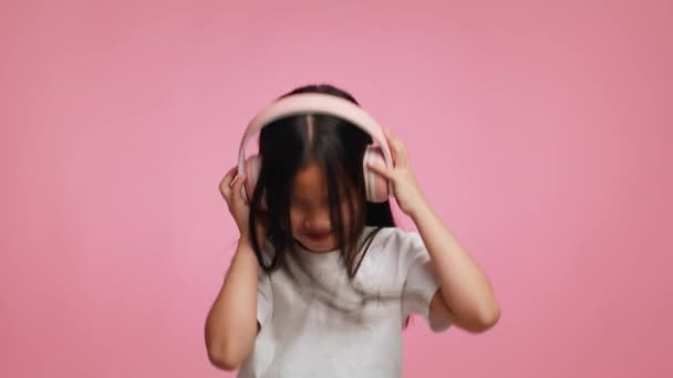 Japonesa chica usando auriculares escuchar música bailando en rosa fondo — Vídeo de stock