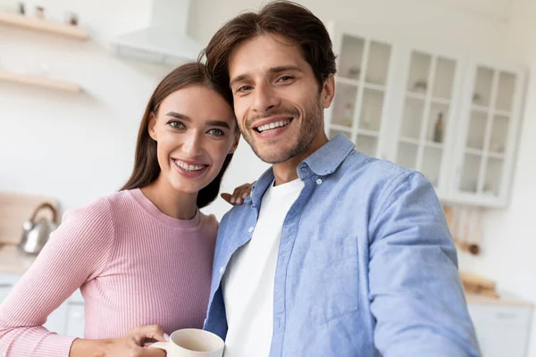 Feliz millennial europeo mujer y chico con tazas, beber café por la mañana y tomar selfie —  Fotos de Stock