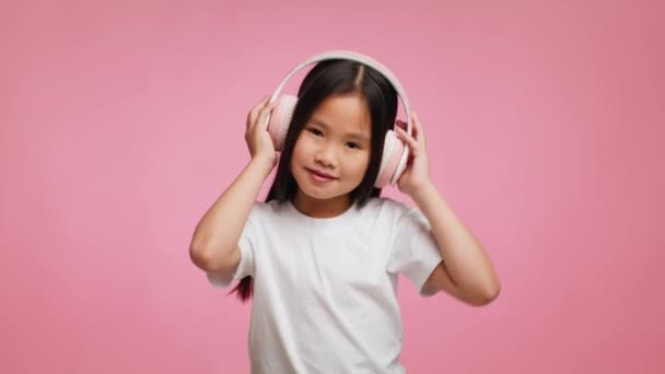 Κορεάτισσα Kid Girl ακούγοντας μουσική φορώντας ακουστικά πάνω από ροζ φόντο — Αρχείο Βίντεο