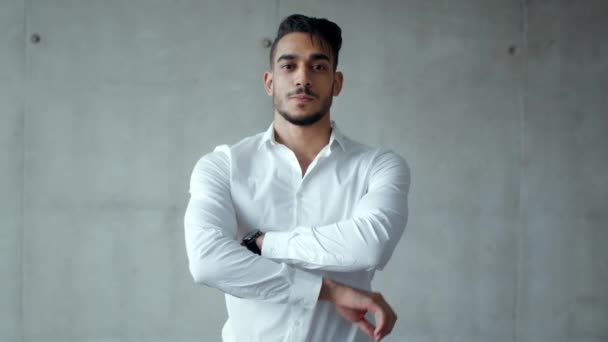 Jonge zelfverzekerde Arabische zakenman in formeel shirt glimlachend naar de camera, poseren met gekruiste handen, grijze muur, slow motion — Stockvideo