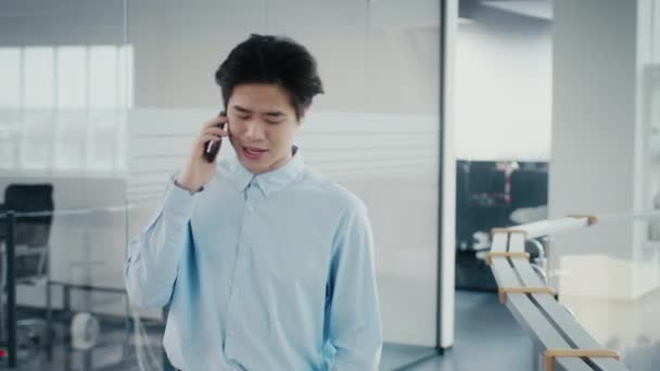 Asiatisk forretningsmand taler på mobiltelefon walking i kontor indendørs – Stock-video