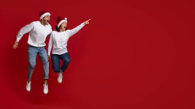 Harika bir teklif. Noel Baba Şapkalı Şaşkın Genç Çift Zıplıyor ve Yandan İşaret Ediyor