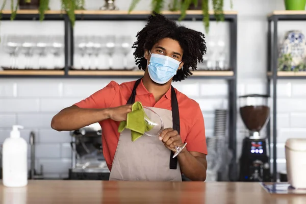 Trabalho durante a pandemia. Jovem barman preto usando máscara médica em pé no balcão do bar — Fotografia de Stock