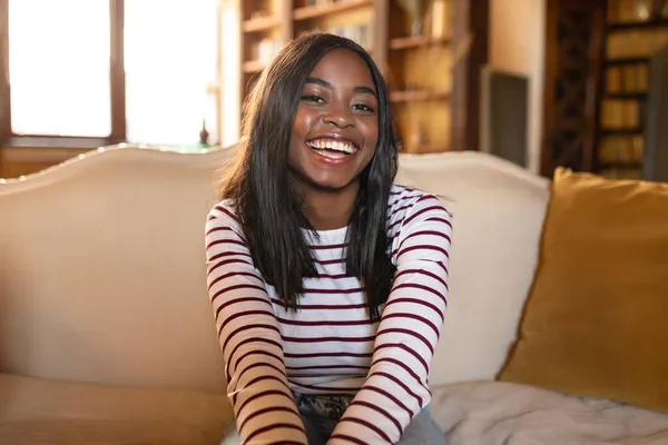 Retrato de la joven mujer afroamericana feliz sonriendo a la cámara, sentada en el sofá en casa — Foto de Stock