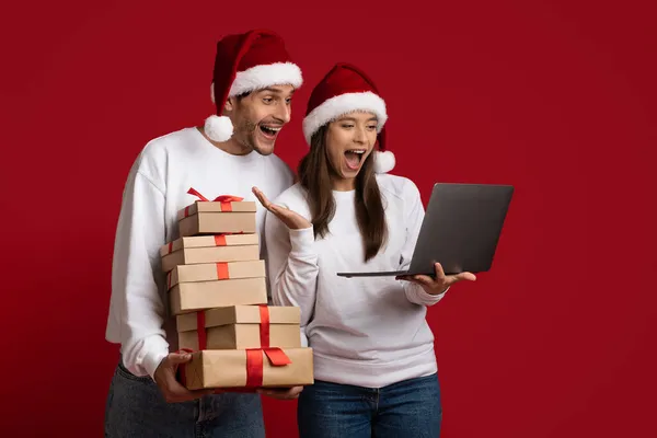 Vente en ligne. Couple excité tenant des boîtes-cadeaux et regardant l'écran d'ordinateur portable — Photo