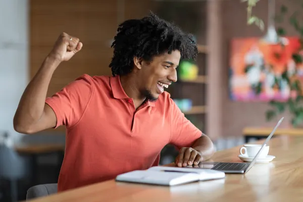 Buone notizie. Uomo nero emotivo guardando lo schermo del computer portatile e celebrando il successo — Foto Stock