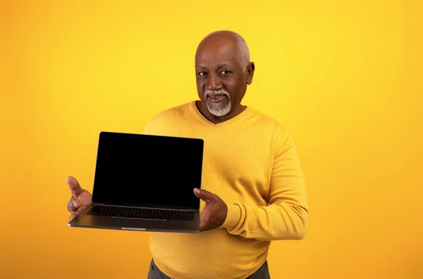 Portrét šťastného staršího černocha demonstrující notebook s prázdnou obrazovkou, pózující na oranžovém pozadí studia, maketa — Stock fotografie
