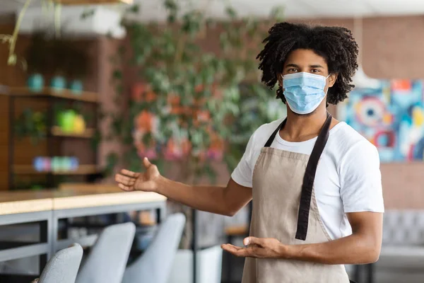 Jovem Barista Preto vestindo máscara médica protetora em pé ao ar livre no café — Fotografia de Stock