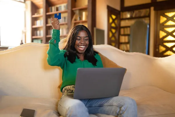 Aufgeregte schwarze Frau mit Laptop und Kreditkarte freut sich über Rabatt im Online-Shop, Einkauf von zu Hause aus — Stockfoto