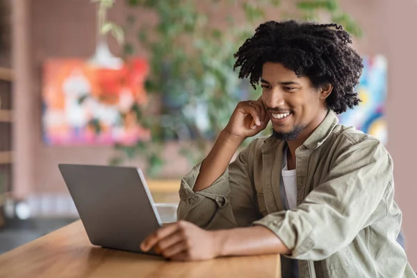 Glada unga svarta killen koppla av med laptop vid bordet i Café — Stockfoto