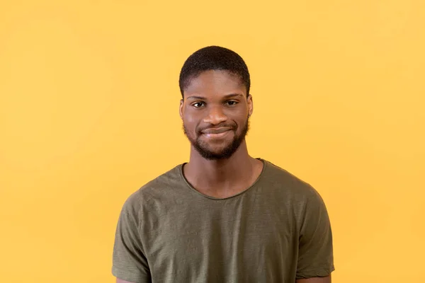 Bello africano americano barbuto uomo guardando e sorridendo alla macchina fotografica, indossando t-shirt, posa su sfondo giallo — Foto Stock