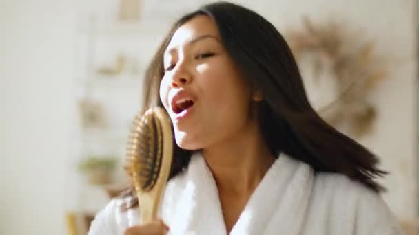 Webcam pov portret van jonge speelse aziatische vrouw zingen om camera met haarborstel, doen alsof ze popster thuis — Stockvideo