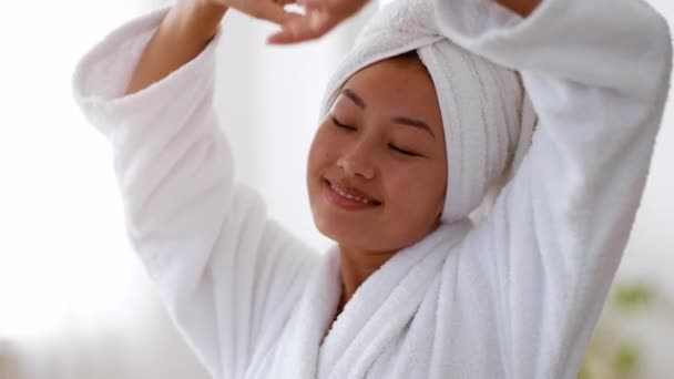 Jeune dame asiatique paisible bien reposé étirant son corps, jouissant après la douche bien-être dans la salle de bain, portant un peignoir — Video