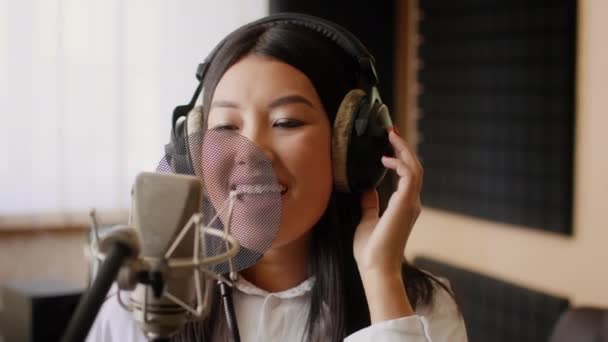 Энергичная молодая азиатская вокалистка поет в микрофоне в музыкальной студии — стоковое видео