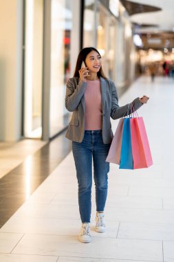 Alışveriş çantalı güzel bir Asyalı kadın süpermarkette yürüyor, cep telefonuyla konuşuyor.