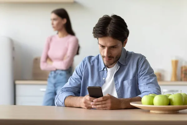 Elfoglalt Y-generációs európai srác játszik a játék okostelefon, és figyelmen kívül hagyja a sértett feleség a konyhában — Stock Fotó