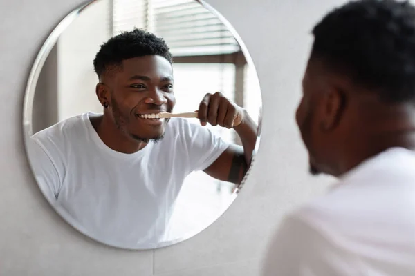 Africano chico limpieza dientes sonriendo a en espejo en cuarto de baño — Foto de Stock