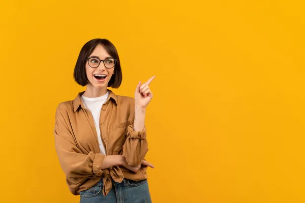 Überglückliche junge Frau zeigt mit dem Finger zur Seite Werbetext steht über gelbem Studiohintergrund, leerer Raum — Stockfoto