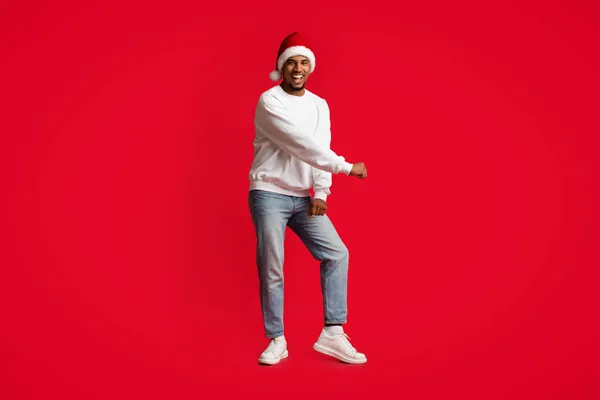 Noel Baba şapkalı neşeli Afrikalı Amerikalı adam kırmızıda dans ediyor. — Stok fotoğraf