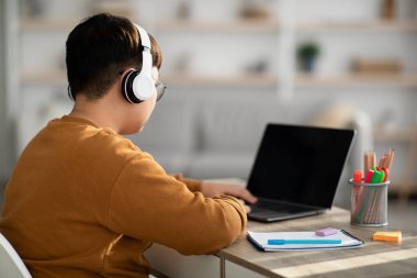 Çinli çocuk boş ekranlı ve kulaklıklı laptop kullanıyor.