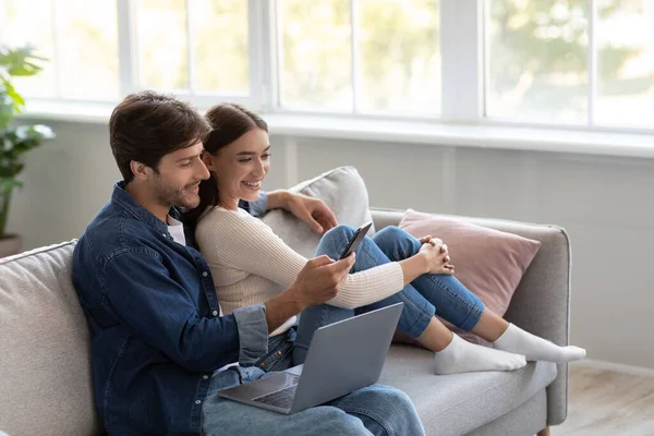 Feliz millennial europeo masculino y femenino mirar el teléfono inteligente y llamar en línea en el interior de la sala de estar —  Fotos de Stock