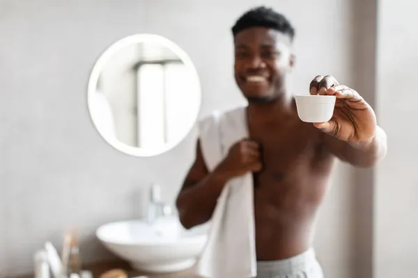 Uomo afroamericano che mostra crema idratante vaso in bagno — Foto Stock