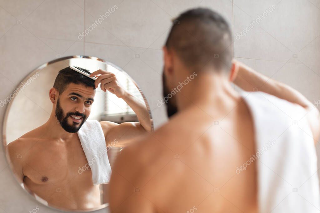 Back rear view of guy looking in mirror brushing hair