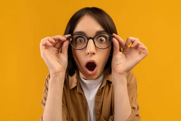 Incroyable. Choqué dame caucasienne touchant des lunettes et regardant la caméra en état de choc, posant sur fond jaune — Photo