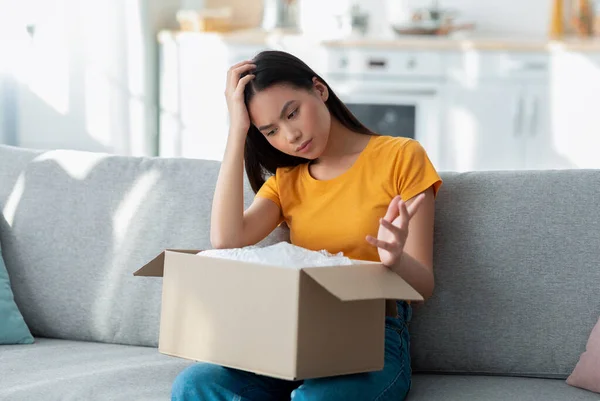 Paquete dañado. Decepcionado asiático señora unboxing su entrega, mirando dentro de caja, infeliz debido a error de envío — Foto de Stock