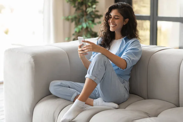 Porträtt av glad ung kvinna med hjälp av smartphone, sitter på bekväm soffa hemma, kopiera utrymme — Stockfoto