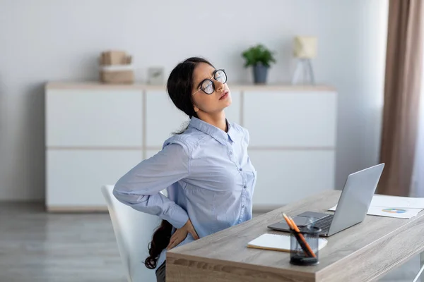 Stanco sconvolto giovane donna d'affari indiana che soffre di mal di schiena, spasmo muscolare sul posto di lavoro con laptop — Foto Stock