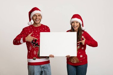 Noel Reklamı. Noel Baba şapkalı ve kazaklı çift boş tabelayı işaret ediyor.