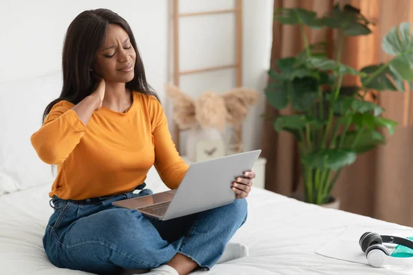 Mujer joven africana tocando el cuello Aching usando el ordenador portátil en casa —  Fotos de Stock