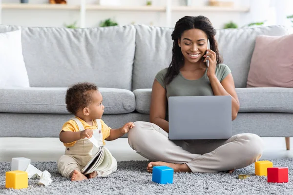 Черная женщина работает над ноутбуком и заботится о своем младенце — стоковое фото