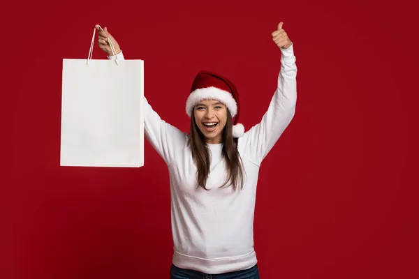 Super offre. Femme gaie dans Santa Hat tenant blanc blanc sac à provisions — Photo