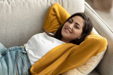 Haftasonu evde tembellik. Rahat bir Arap kadın, elleri başının arkasında uzanıyor ve kameraya gülümsüyor.