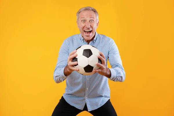 Dojrzały mężczyzna pozowanie z piłką nożną na żółtym tle — Zdjęcie stockowe
