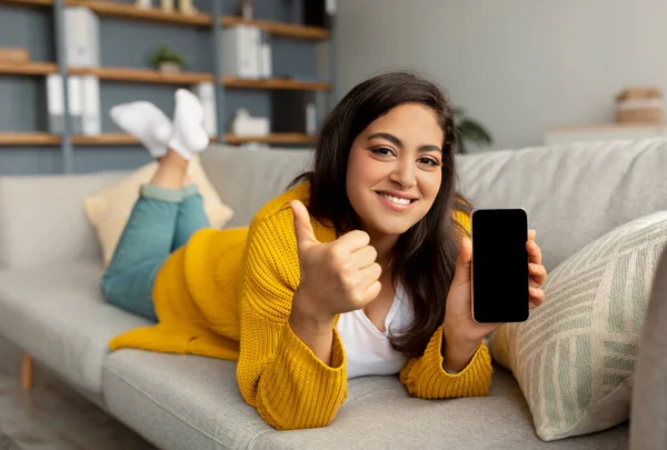 Guarda questa app per dispositivi mobili. Felice signora araba dimostrando smartphone con schermo bianco e mostrando pollice in su — Foto Stock